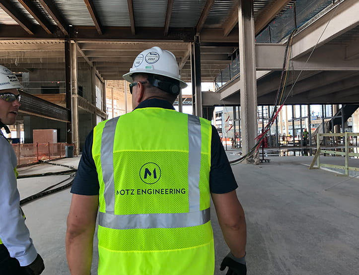 Construction worker wearing a hard hat and high-visibility Motz Engineering vest inside an unfinished building