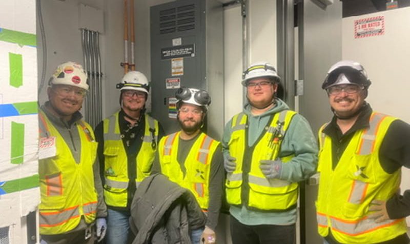Motz Engineering workers wearing hard hats and safety vests in an electrical utility room