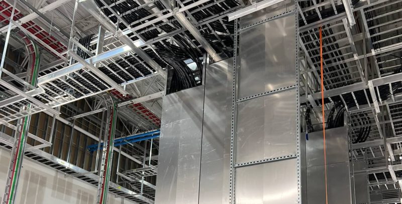Overhead cable trays with thick black cables and vertical metal ducting suspended from ceiling framing