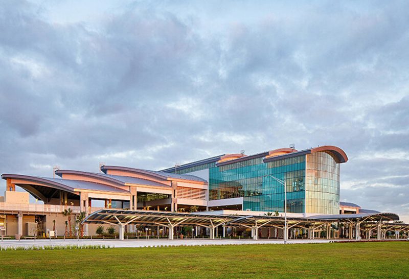 Exterior of a modern multi-level terminal with curved roofs, glass walls, and covered drop-off walkways