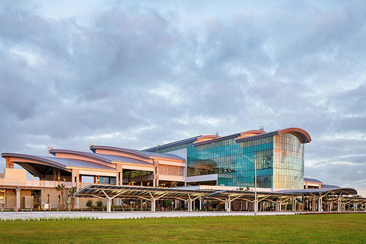 Exterior of a modern multi-level terminal with curved roofs, glass walls, and covered drop-off walkways